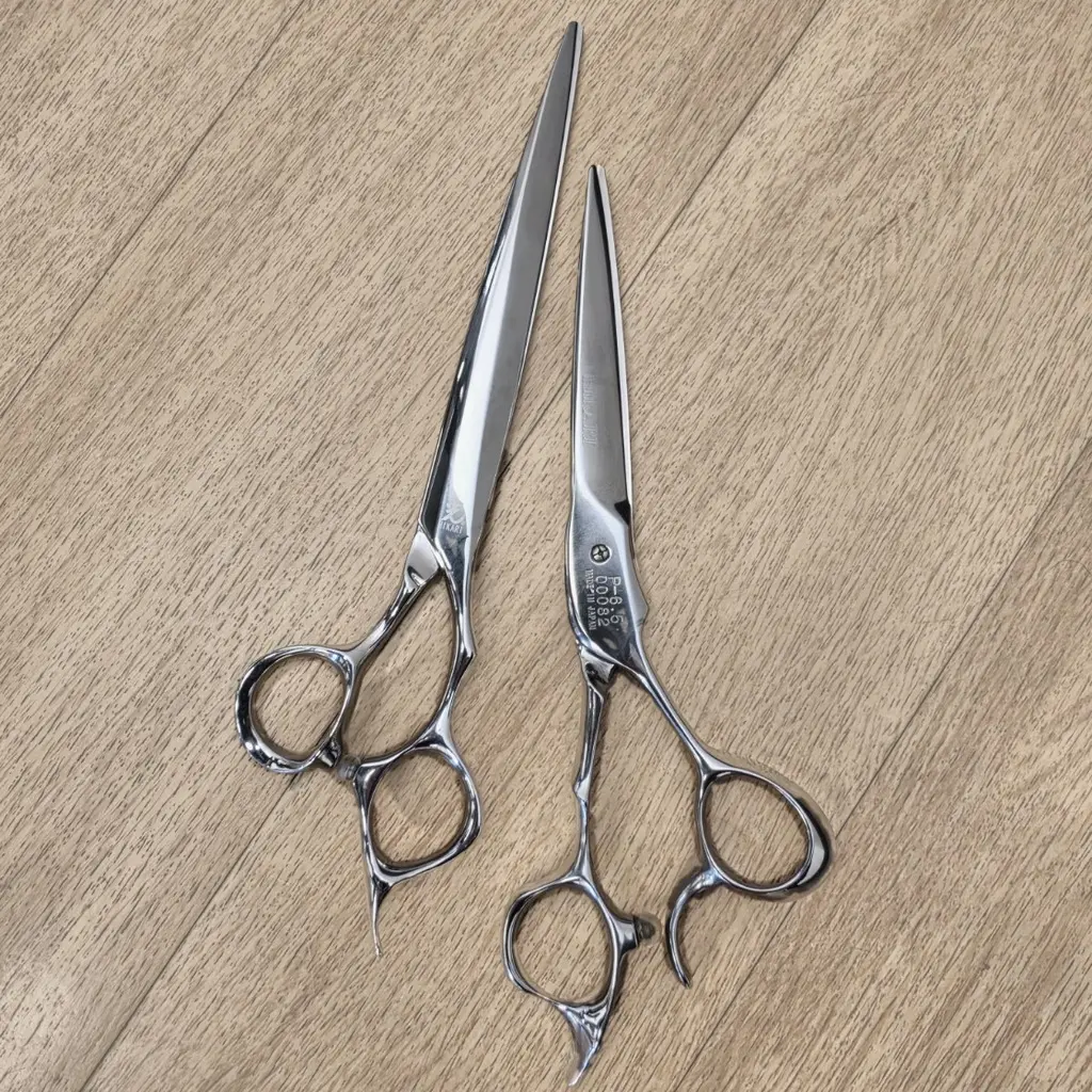 Two pairs of Frank's stainless haircutting shears on a honey wood floor